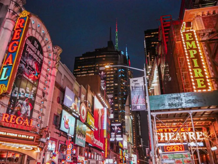 Bright neon signs and billboards light up a busy street at night in Times Square, New York City, creating the perfect backdrop for any Times Square New York itinerary, with theaters, shops, and tall buildings adding to the lively atmosphere.